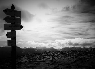 Black and white image of cloudy mountainous scenery and sign post indicating various directions
