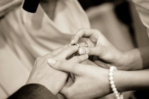 Black and white image of couple exchanging wedding rings