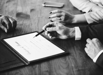 Black and white photo of couple signing a pre-nuptial agreement in front of a witness