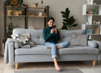 Happy woman sitting on sofa and looking at iPhone