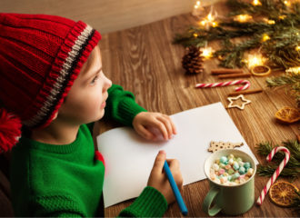 Child wearing woolly red hat writing letter to Santa - cup of hot chocolate with marshmallows