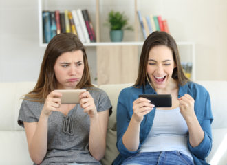 Happy girl next to upset girl looking at mobile phones